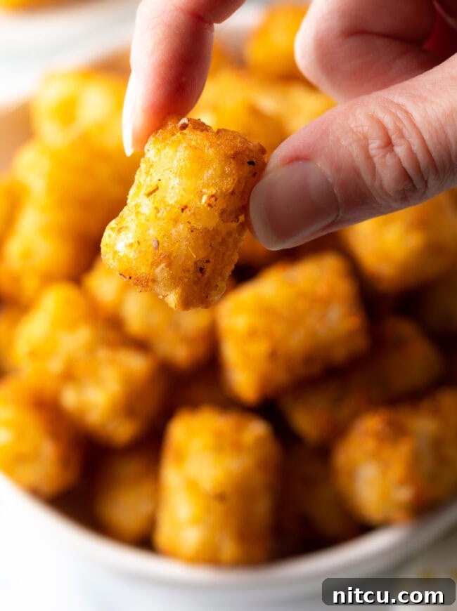 Hand holding crispy tater tot close to camera.