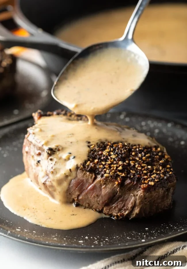 Peppercorn-Crusted Steak with Velvety Cognac Sauce 2 Spoon pouring cognac cream sauce over steak au poivre on a plate.