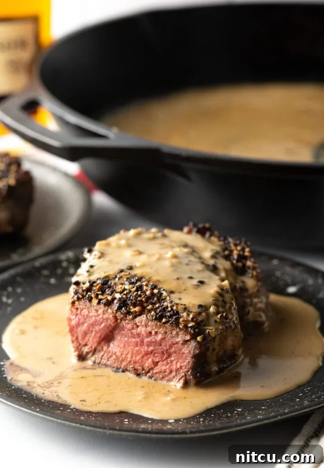 Peppercorn-Crusted Steak with Velvety Cognac Sauce 12 Steak on plate with cream sauce, bite taken to show medium rare cook on the inside.