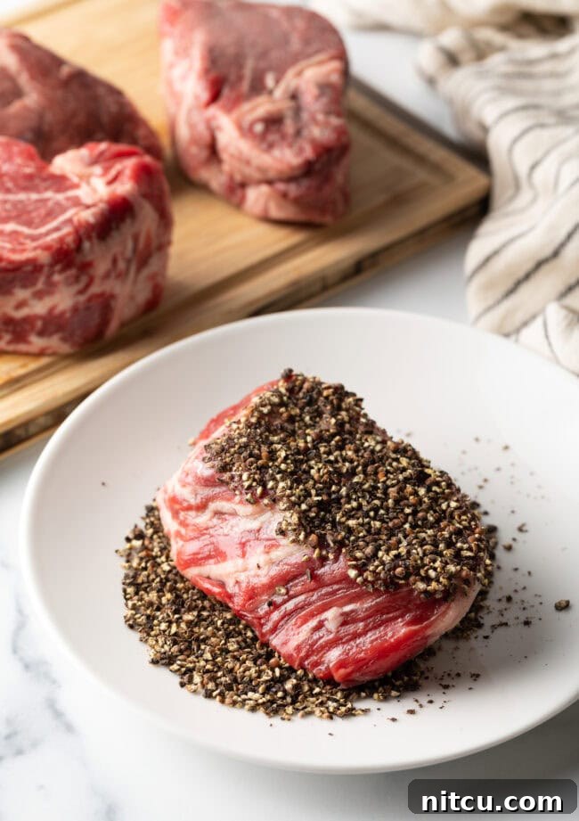 Peppercorn-Crusted Steak with Velvety Cognac Sauce 6 Uncooked steak being crusted in coarse black ground peppercorns on a plate.
