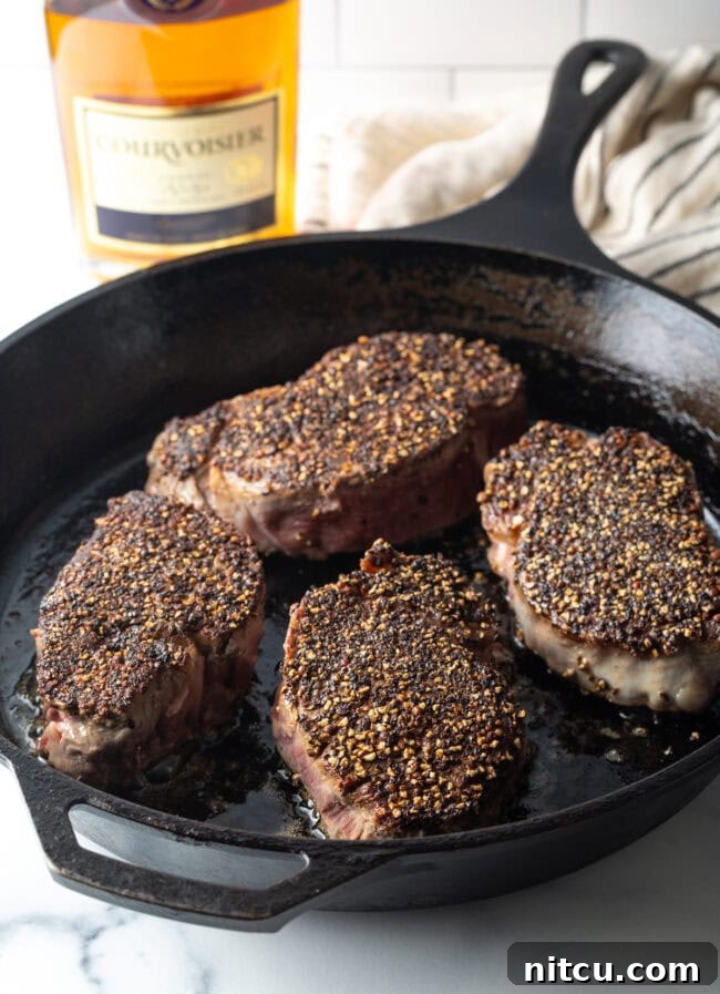 Peppercorn-Crusted Steak with Velvety Cognac Sauce 7 Steaks with pepper crust being seared in a cast iron skillet.