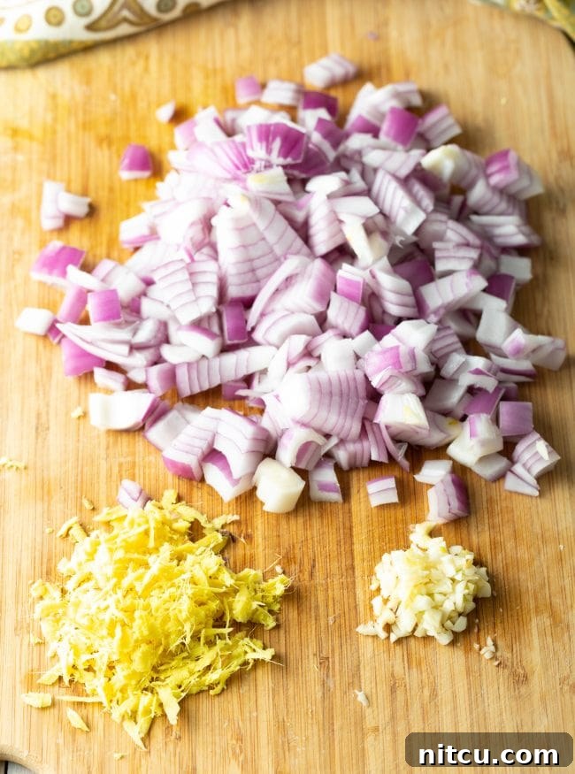 Flavors of Ethiopia 4 Ingredients for Misir Wot laid out on a cutting board, including red lentils, onions, garlic, ginger, and spices, awaiting preparation.