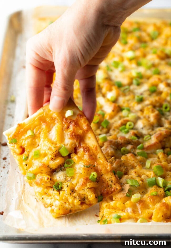 Cheesy Mac Pizza 12 Hand lifting piece of mac and cheese pizza from full pizza.