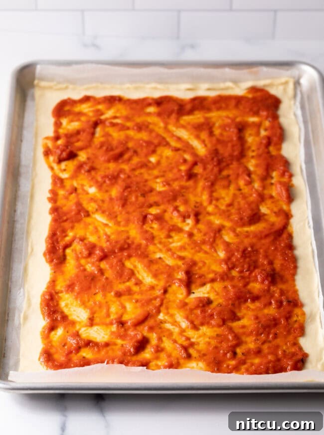 Cheesy Mac Pizza 6 Dough rolled out in a rectangle with pizza sauce spread on top.