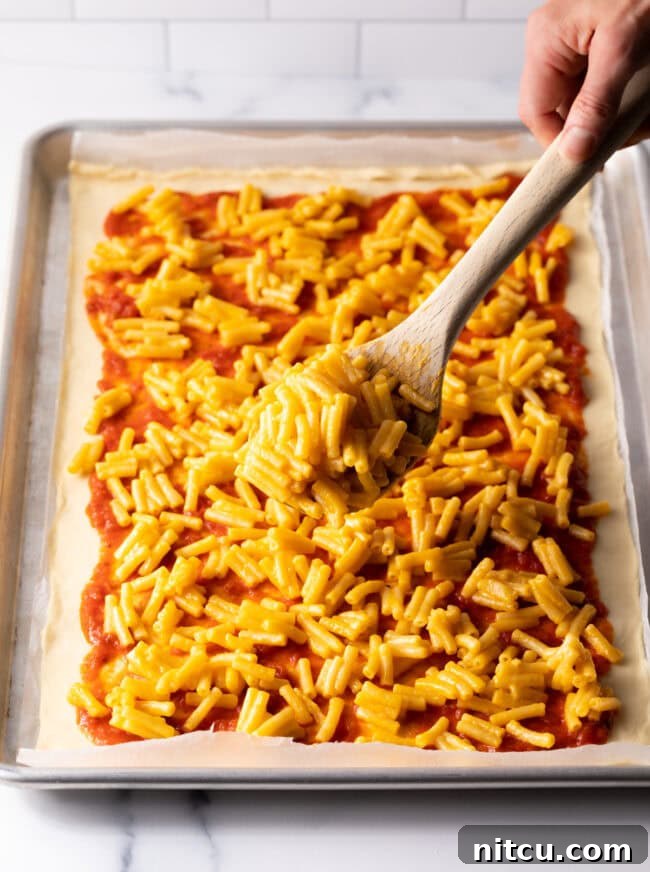Cheesy Mac Pizza 7 Cooked mac and cheese being spread over pizza sauce on dough.