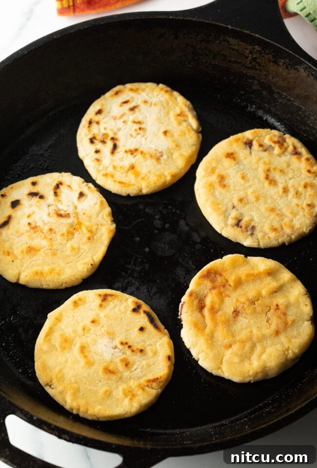 Homemade Pupusas 16 Pupusas cooking and sizzling in a cast iron skillet.