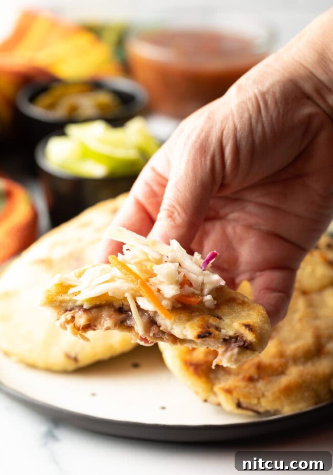 Homemade Pupusas 20 Hand holding a pupusa with a bite taken out, topped with curtido.
