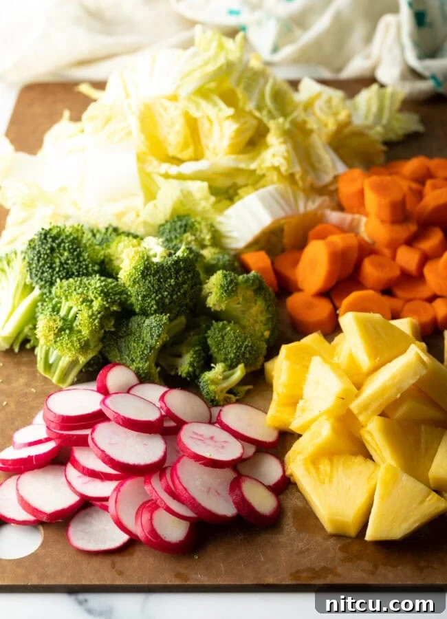 Simply Delicious Chicken Teriyaki Bowl 5 Fresh chopped veggies on a cutting board: broccoli, cabbage, carrots, pineapple, radishes.