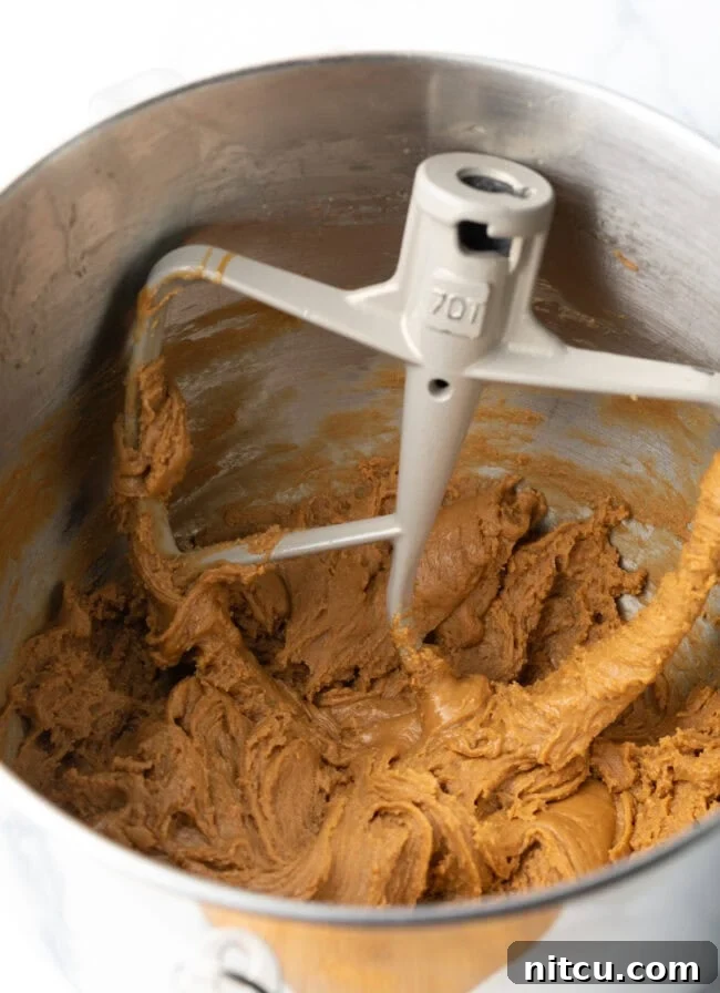 Creamy Maple Walnut Delight 8 A standing mixer bowl with the paddle attachment, containing the maple fudge mixture that has begun to crystallize and lighten in color.