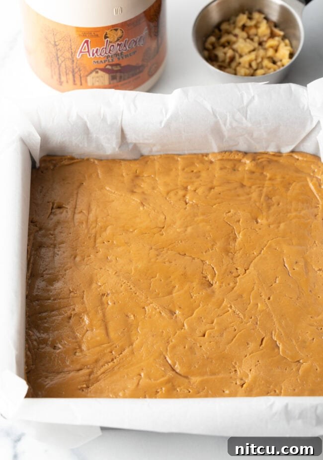 Creamy Maple Walnut Delight 9 Smooth maple fudge mixture pressed firmly into a square baking pan lined with parchment paper, ready for chilling.