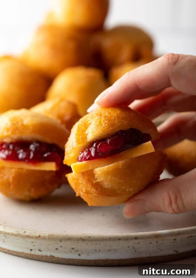 Decadent Cake Creation 13 A hand holding a small Vetkoek (fat cake) fried dough, cut open and filled with vibrant cheese and jam.