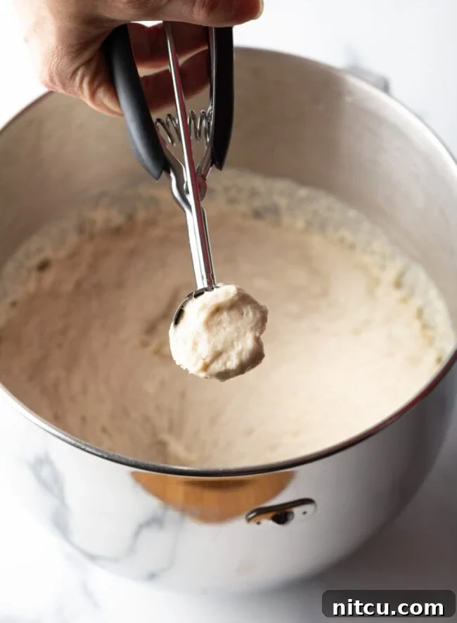 Decadent Cake Creation 7 A hand using a 2-tablespoon scoop to portion out wet dough for frying.