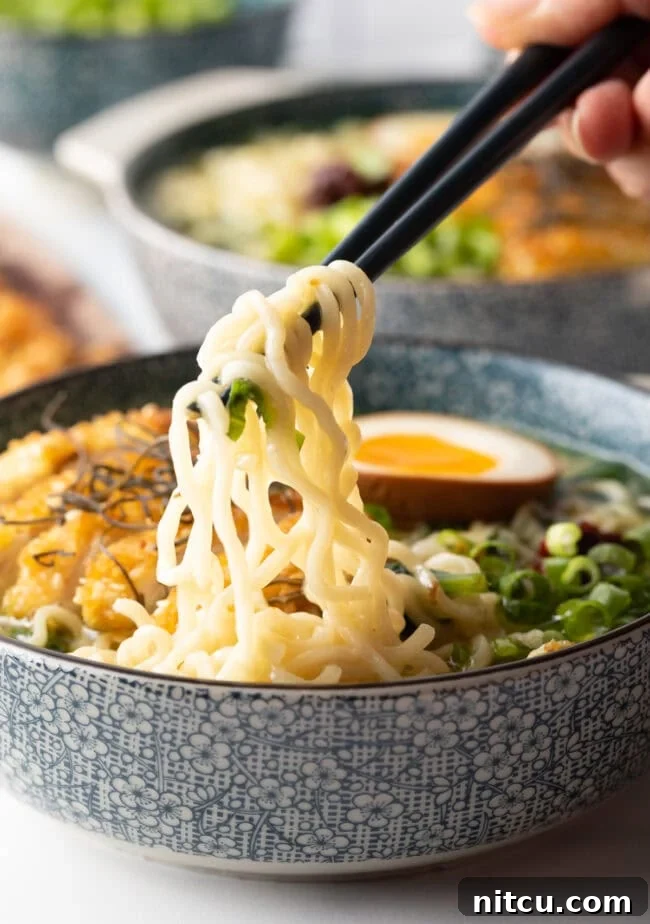 Golden Katsu Ramen 14 Hand with chopsticks, pulling noodles out of a soup bowl filled with katsu ramen.