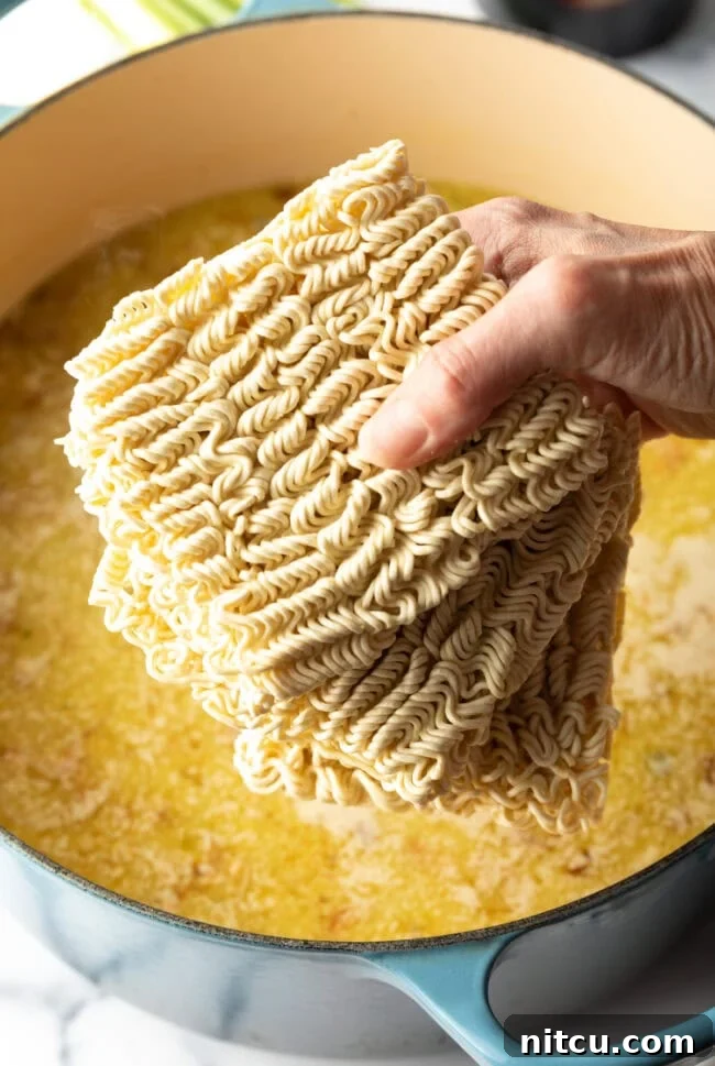 Golden Katsu Ramen 9 Hand holding blocks of ramen noodles above pot of boiling water.
