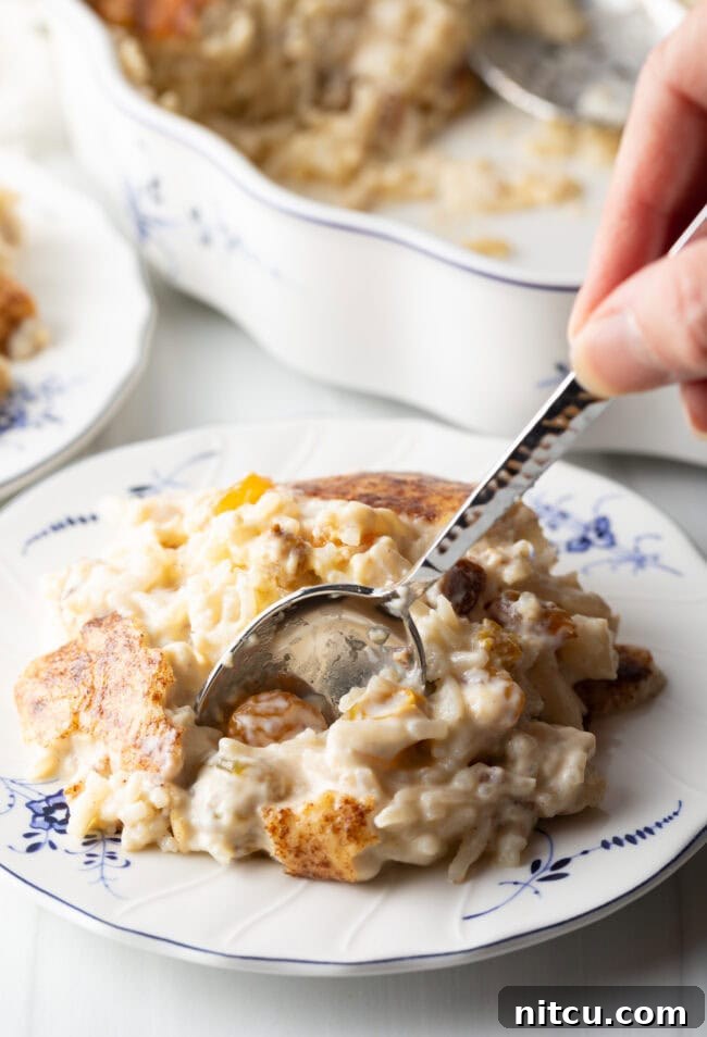 Golden Baked Rice Pudding 11 A metal spoon delicately scooping a bite of luscious rice pudding from a white plate, highlighting its creamy texture and comforting appeal.