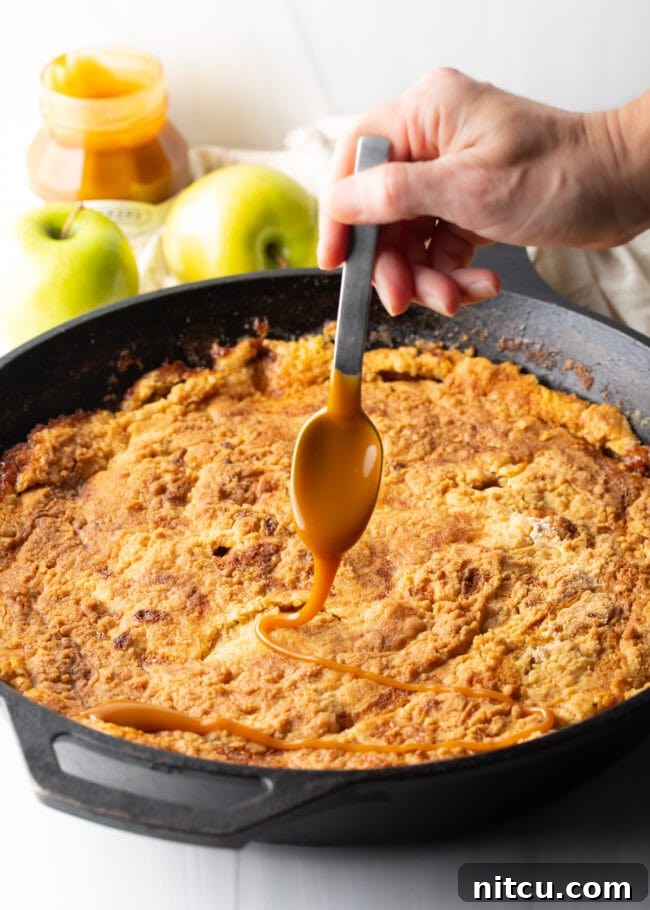 Gooey Caramel Apple Bake 11 A hand holds a spoon, artfully adding a stream of thick, luscious caramel sauce over the warm, baked skillet of apple dump cake.