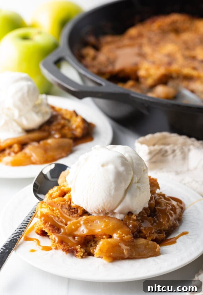 Gooey Caramel Apple Bake 13 A charming scene of a portion of Caramel Apple Dump Cake on a white plate, accompanied by a scoop of vanilla ice cream and a spoon, inviting a delicious bite.