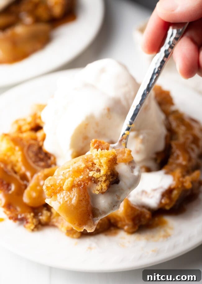 Gooey Caramel Apple Bake 14 A spoon holds a perfect bite of warm Caramel Apple Dump Cake, presenting it enticingly towards the camera.