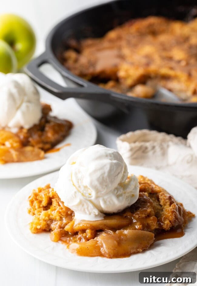 Gooey Caramel Apple Bake 4 A delectable portion of Caramel Apple Dump Cake artfully presented on a white plate, accompanied by a generous scoop of creamy vanilla ice cream.