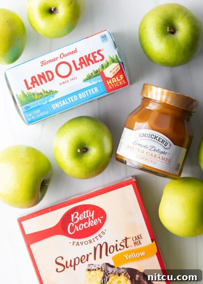Gooey Caramel Apple Bake 5 A vibrant top-down view of the core ingredients for Caramel Apple Dump Cake: sticks of unsalted butter, crisp Granny Smith apples, a jar of salted caramel sauce, and a box of classic yellow cake mix.
