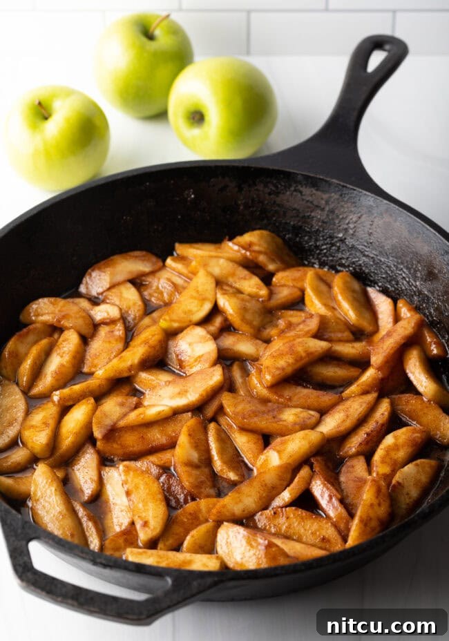 Gooey Caramel Apple Bake 7 Perfectly cooked and spiced apple slices shimmer invitingly in a cast iron skillet, forming the delicious base of the dump cake.