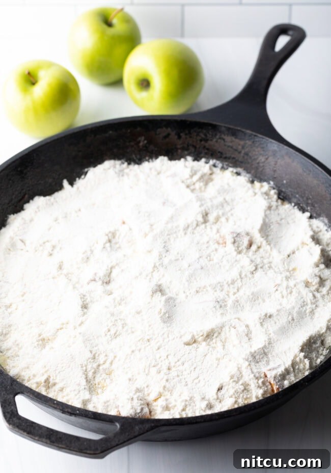 Gooey Caramel Apple Bake 8 Dry powdered cake mix evenly sprinkled over the softened, spiced apple filling in a cast iron skillet, ready for butter and baking.