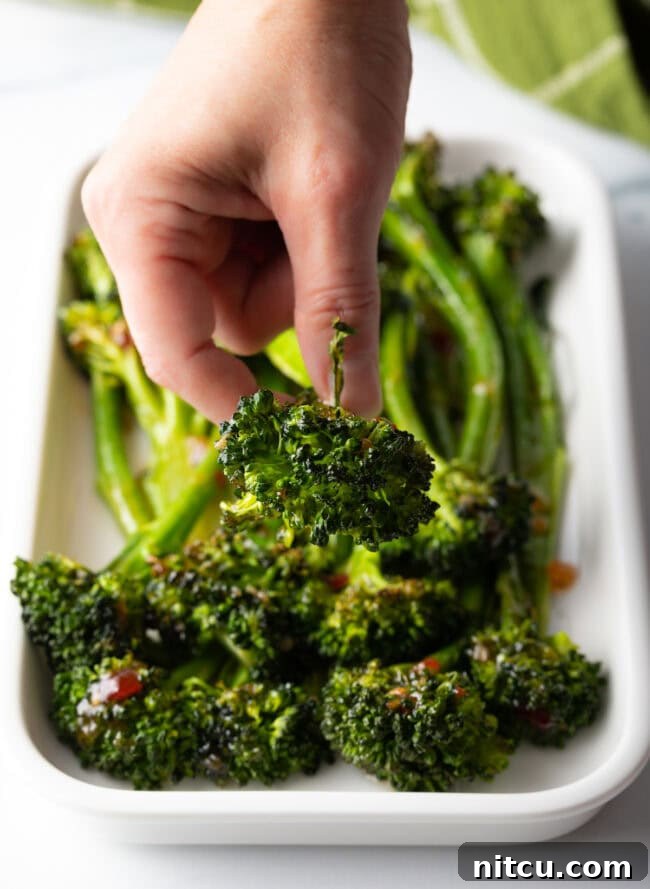 Roasted Broccolini with Chili Honey Glaze 9 Hand holding piece to the camera, floret head-first.