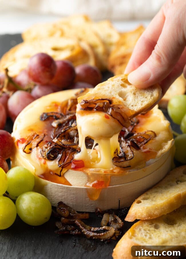 Gooey Baked Camembert Delight 14 Hand scooping gooey melted cheese with onions and chili sauce from the baked wheel.