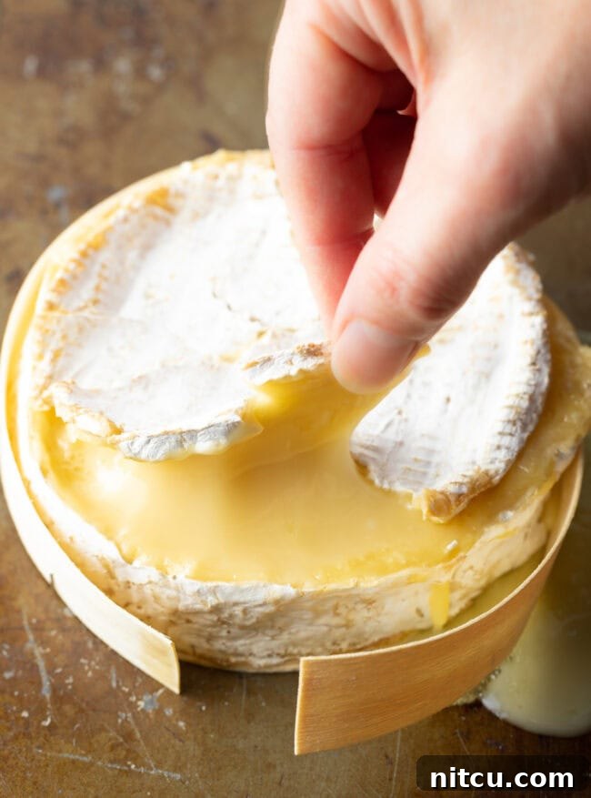 Gooey Baked Camembert Delight 9 Hand peeling back the top rind. on the camembert cheese.