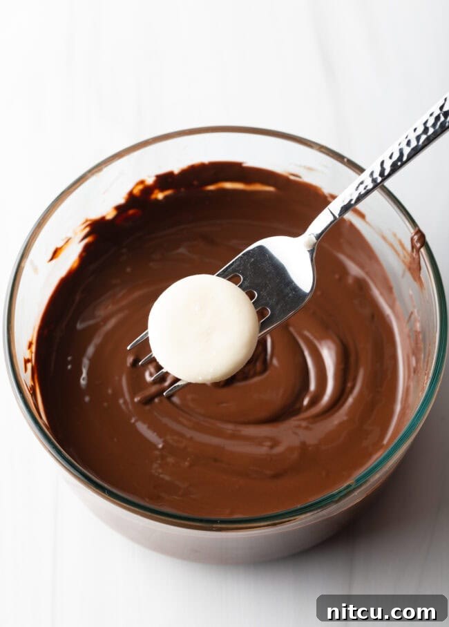 Refreshing Homemade Peppermint Delights 8 Fork with white dough disc hovering above a glass bowl of melted chocolate.