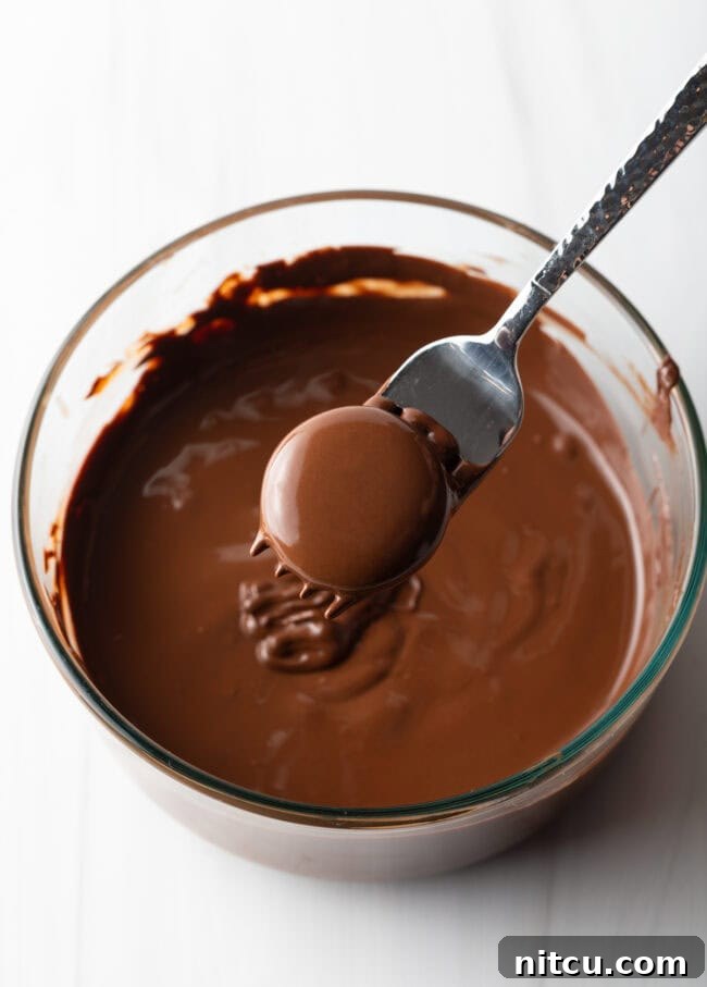 Refreshing Homemade Peppermint Delights 9 Fork with chocolate-coated candy, hovering above bowl of melted chocolate.