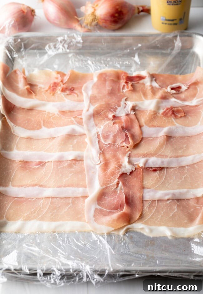 Slices of prosciutto laid out on plastic wrap.