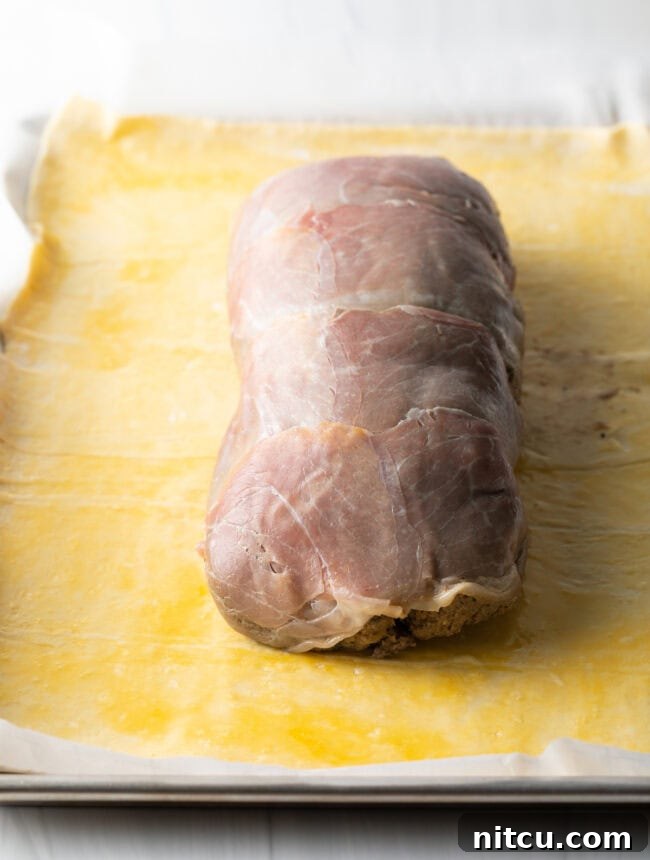 Wrapped beef tenderloin placed in the center of rolled out puff pastry on a baking dish. 