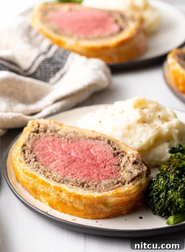 Final shot from Beef Wellington Recipe, close view of slice on plate with sides.