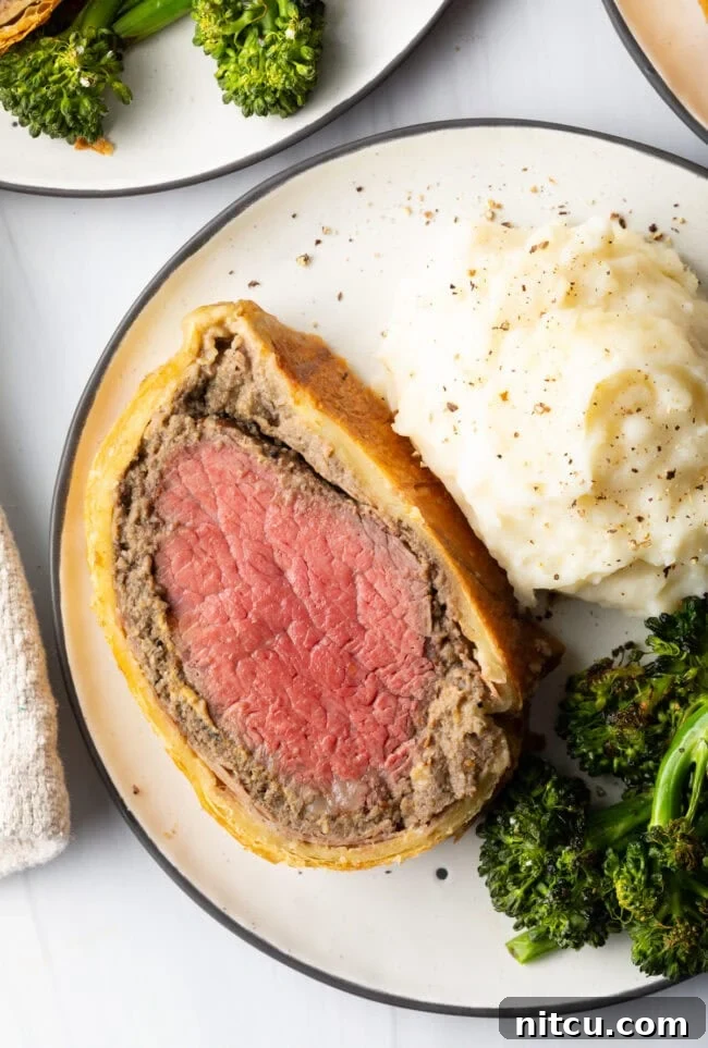 Top down slice of our best beef wellington recipe on a plate with mashed potatoes and roasted broccoli.