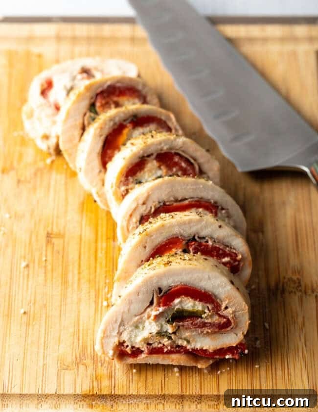 Savory Stuffed Chicken Rolls 12 Stuffed chicken roulade, thin sliced on a cutting board with large knife, revealing the beautiful filling inside.