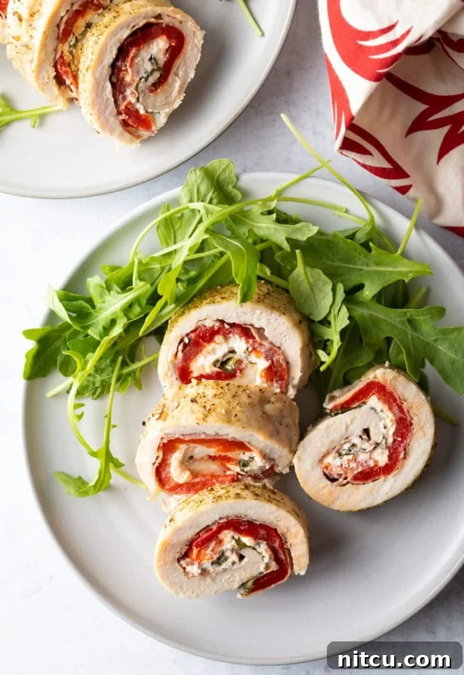 Savory Stuffed Chicken Rolls 3 Top down view of slices of stuffed chicken roulade on a white plate with fresh arugula, highlighting the colorful filling.