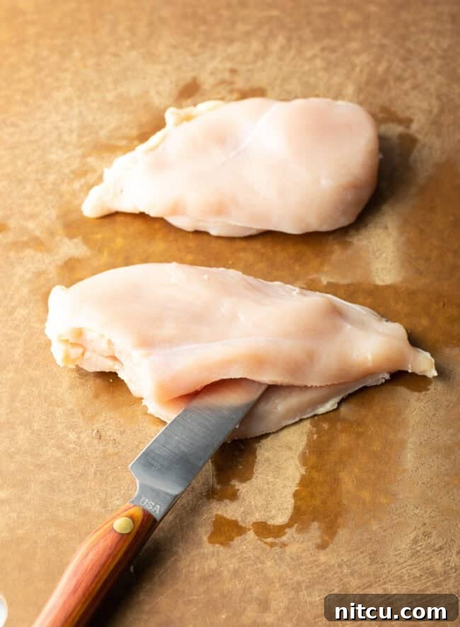 Savory Stuffed Chicken Rolls 4 Large knife slicing raw chicken breast in half width-wise, demonstrating the butterflying technique.