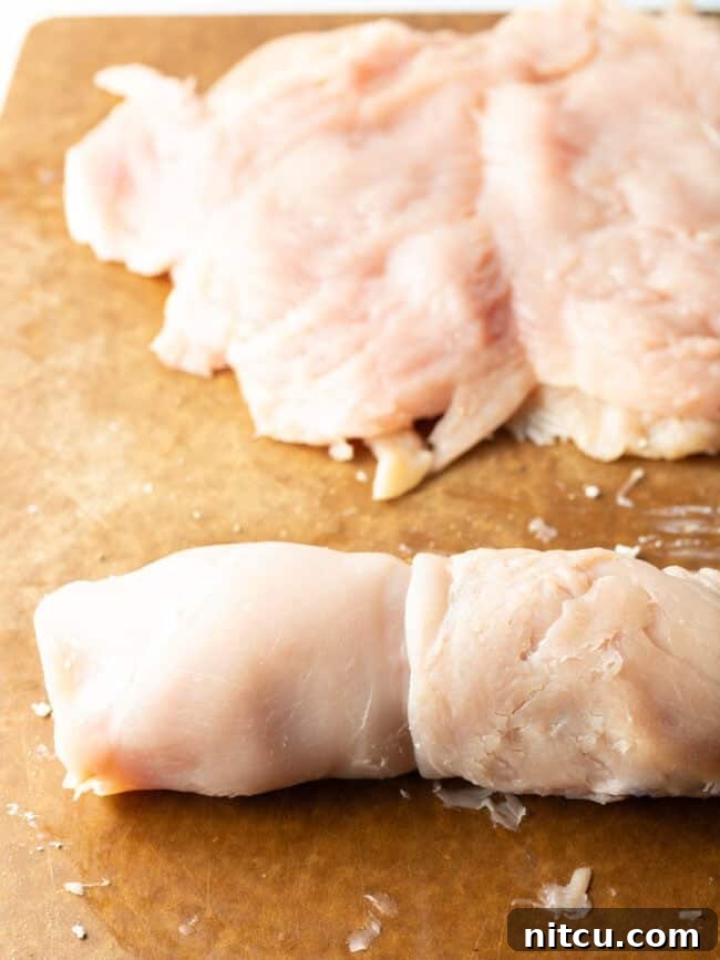 Savory Stuffed Chicken Rolls 9 Stuffed raw chicken rolled on a cutting board, wrapped with twine for secure baking.