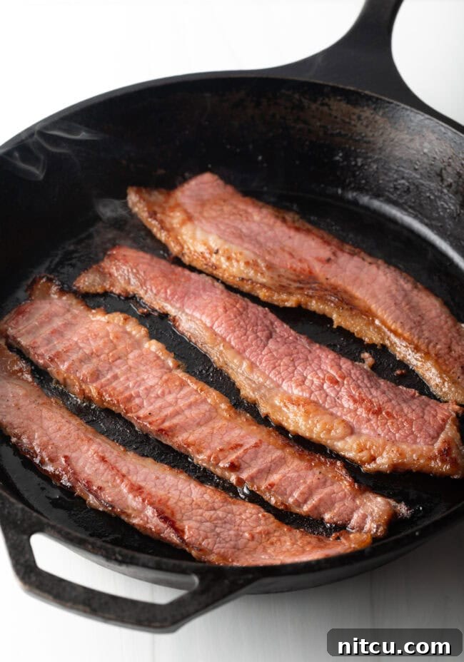Perfect Homemade Beef Bacon 9 Overhead shot of 4 pieces of beef bacon in a cast iron skillet.