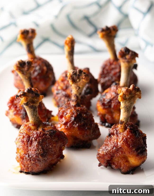 Irresistible Sweet Heat Chicken Lollipops 2 8 chicken lollipop drumettes standing up on a white serving tray.