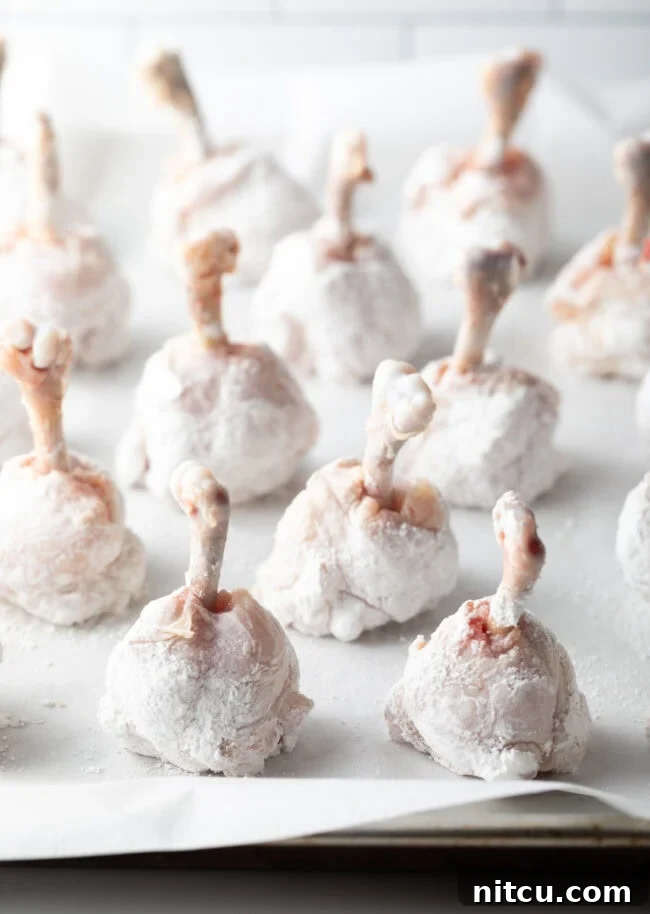 Irresistible Sweet Heat Chicken Lollipops 11 Rows of cornstarch dredged drummies on a baking sheet with parchment paper.