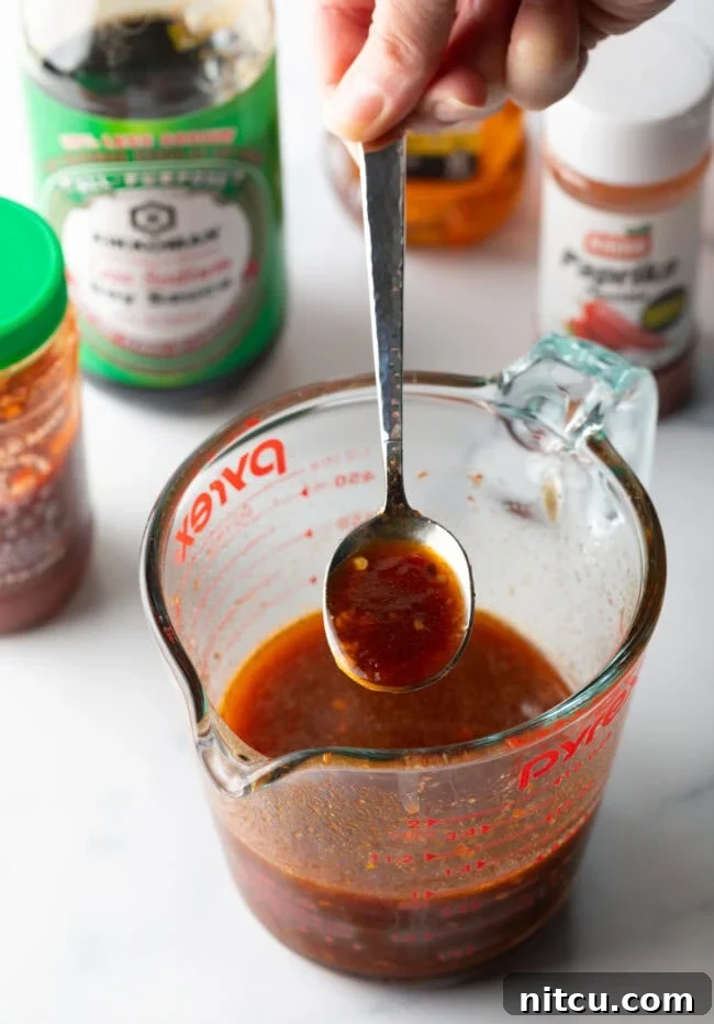 Irresistible Sweet Heat Chicken Lollipops 12 Sweet and spicy sauce made in a glass measuring pitcher, with metal spoon showing spoonful to camera.