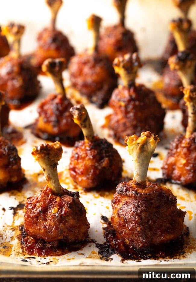 Irresistible Sweet Heat Chicken Lollipops 14 Rows of baked chicken lollipops standing straight up on a baking sheet.