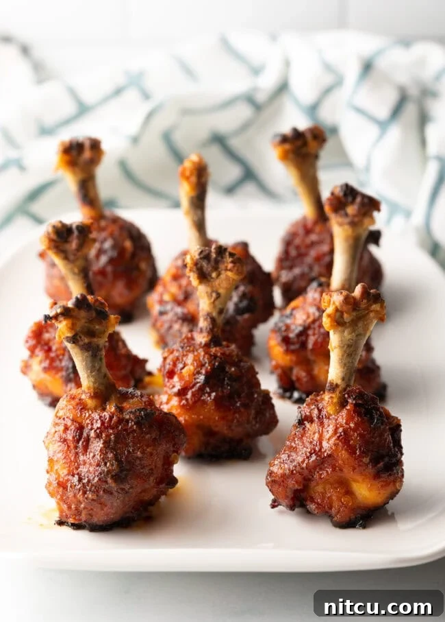 Irresistible Sweet Heat Chicken Lollipops 15 Lollipop chicken drumettes baked and standing in rows on a white serving platter.