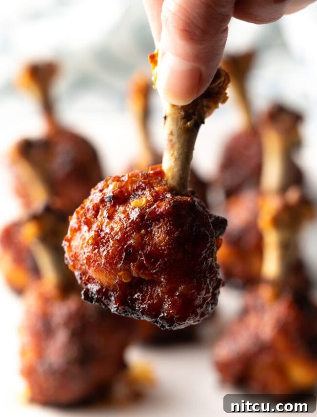 Irresistible Sweet Heat Chicken Lollipops 16 Hand holding final shot of chicken lollipop recipe, drumette to camera.