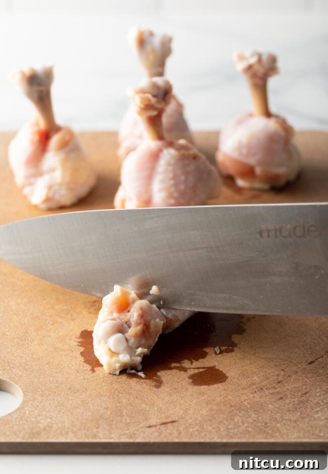 Irresistible Sweet Heat Chicken Lollipops 7 Knife cutting off tip of a drumette on a cutting board.