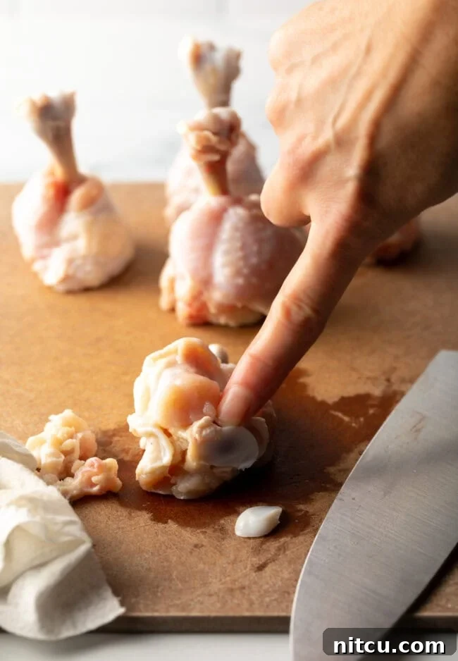 Irresistible Sweet Heat Chicken Lollipops 8 Finger pointing to tip of a drumette on a cutting board.