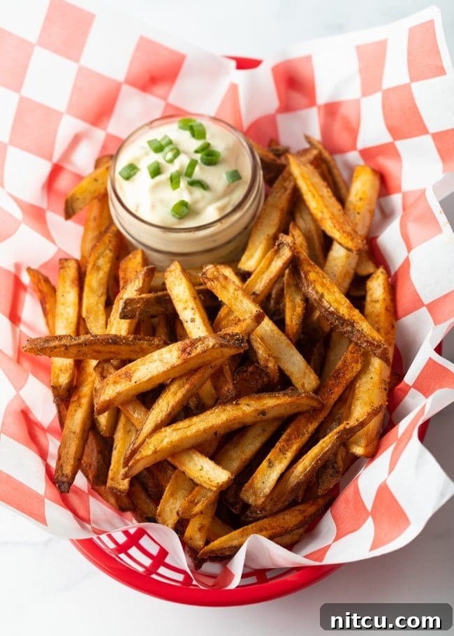 Russet Potatoes Ultimate Recipe and Cooking Tips 13 Top down view Cajun french fries in a white and red checkerboard container, with ramekin of dipping sauce.