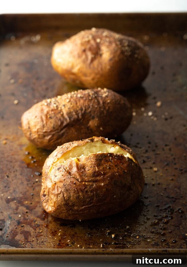 Russet Potatoes Ultimate Recipe and Cooking Tips 6 Three baked potatoes on a baking sheet. One closest to camera is split open at the top.